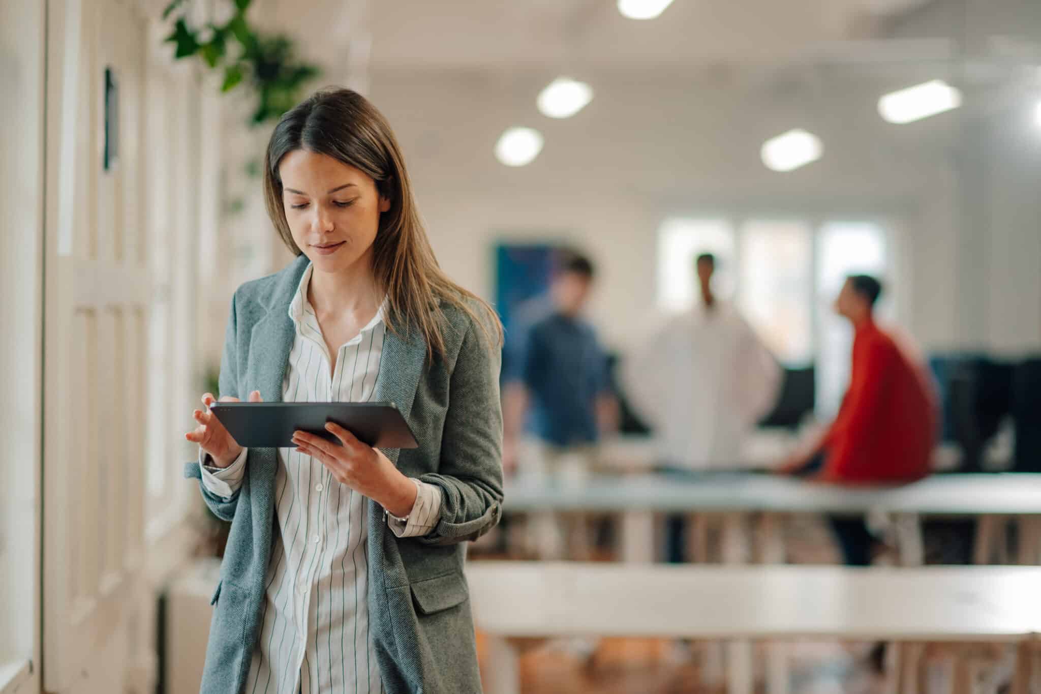 Businesswoman using digital tablet in modern office with colleagues working in background